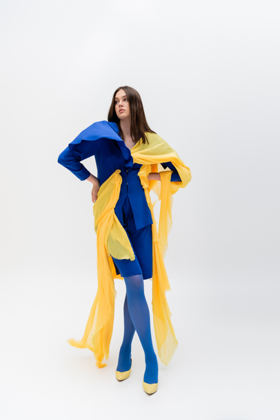 full length of confident ukrainian woman in blue and yellow clothes posing with hands on hips on grey - 写真・画像