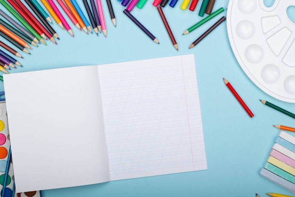 Порожній аркуш косої лінії ноутбука, приладдя для художньої школи для малювання, на синьому фоні з копіювальним простором для тексту. Барвисті олівці, маркери, фарби, олівці. Вид зверху. Назад до школи
 - Фото, зображення