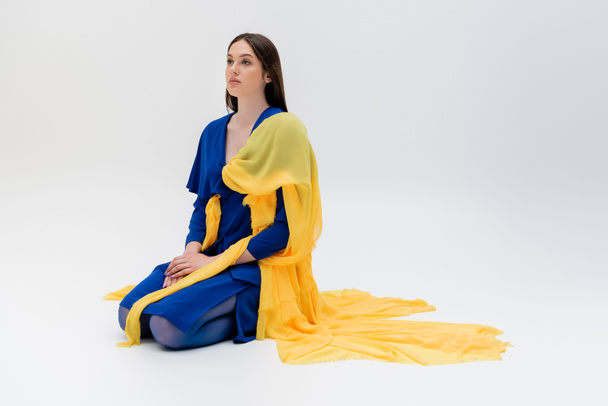 full length of patriotic ukrainian woman in blue and yellow outfit sitting on grey - Foto, Bild