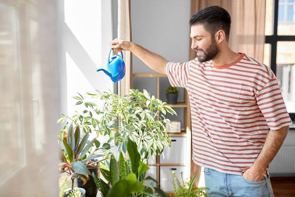 people, nature and plants care concept - happy smiling man watering flowers at home - Foto, Imagem