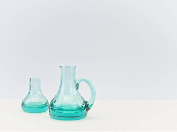 clear green glass bottles on a white table against white wall - Foto, afbeelding