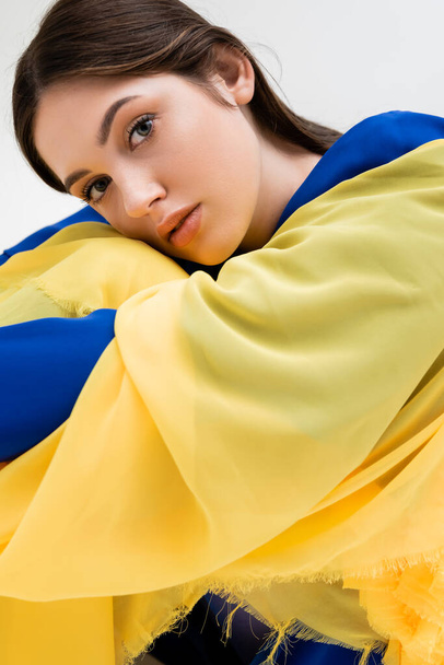 tender ukrainian young woman in blue and yellow outfit looking at camera isolated on grey - Foto, afbeelding