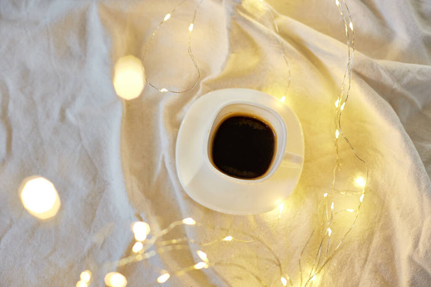 Cup of coffee in bed with a gerlands lights, copy space. Greeting card, romantic breakfast, christmas concept.  - Fotografie, Obrázek
