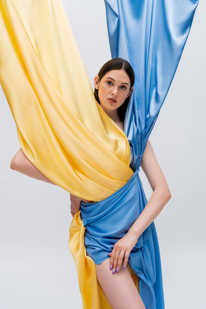 pretty woman in ukrainian blue and yellow dress posing with hand on hip isolated on grey - Φωτογραφία, εικόνα