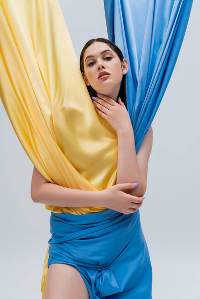 brunette young ukrainian woman in blue and yellow dress isolated on grey - Zdjęcie, obraz
