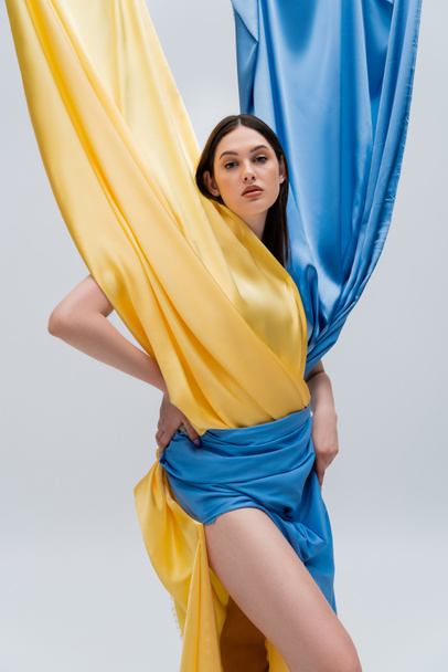 patriotic and young ukrainian woman in blue and yellow dress posing isolated on grey - Foto, Bild