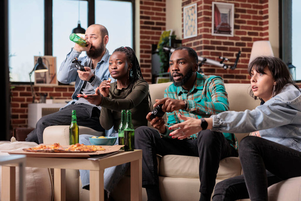 Gruppe verschiedener Freunde, die zusammen Videospiele spielen und sich zu Hause bei Bier und Essen amüsieren. Gaming-Wettbewerb auf der Fernsehkonsole, Menschen jubeln und trinken. - Foto, Bild