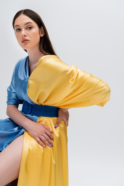 brunette ukrainian woman in blue and yellow dress posing with hand on hip isolated on grey - Foto, Imagem