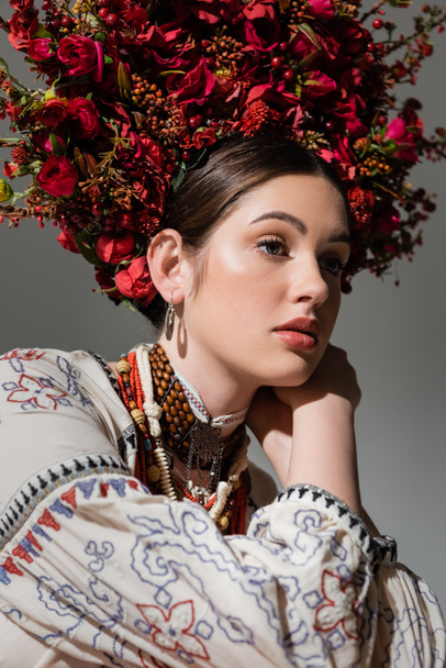 portrait of dreamy ukrainian woman in traditional clothes and floral red wreath isolated on grey - Foto, Imagem