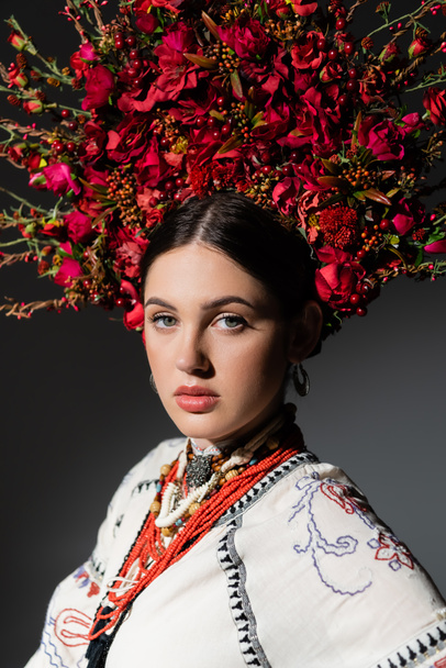 portrait of pretty and young ukrainan woman in floral wreath with red berries isolated on dark grey - Foto, Bild