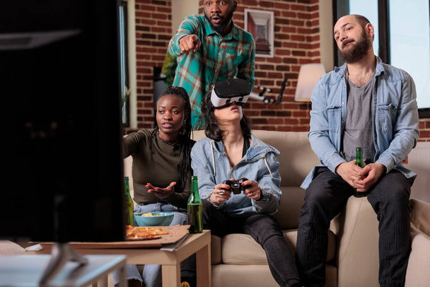 Groupe diversifié d'amis jouant à des jeux vidéo avec des lunettes vr, en utilisant la réalité augmentée et la simulation 3D pour jouer à la compétition. Des gens joyeux appréciant casque et jeu à la fête de la maison. - Photo, image