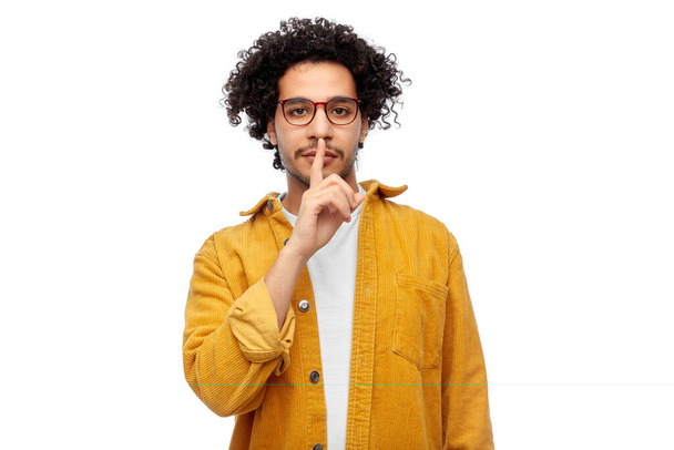 people, silence and confidentiality concept - man in glasses and yellow jacket making hush gesture over white background - Zdjęcie, obraz