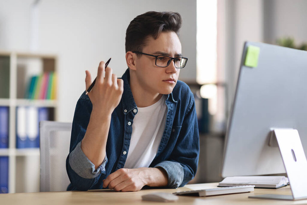 Porträt eines verwirrten männlichen Büroangestellten, der am Arbeitsplatz sitzt und auf den Computerbildschirm blickt, frustrierter Millennial Manager bemerkt Projektfehler bei der Arbeit am Schreibtisch im Büro, Nahaufnahme - Foto, Bild