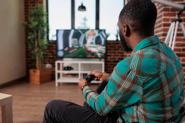 African american man using controller and console to play shooting game, enjoying leisure activity with video games competition. Young adult having fun with shooter gaming strategy. - Fotografie, Obrázek