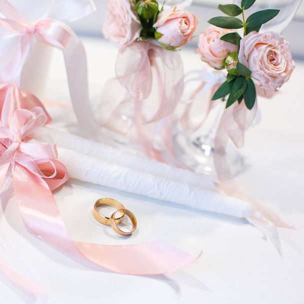 Gold wedding rings lie on the table near the wedding candles. Beautiful wedding background. Wedding details, symbol of love and marriage. - Photo, image