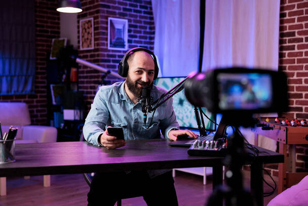 Young man creating podcast content and recording on camera to have lifestyle vlog for social media channel. Influencer using filming and live broadcast equipment in modern studio. - Foto, Bild