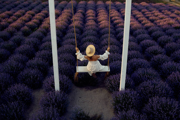 young beautiful pregnant girl on a swing in a lavender field at sunset - Фото, зображення