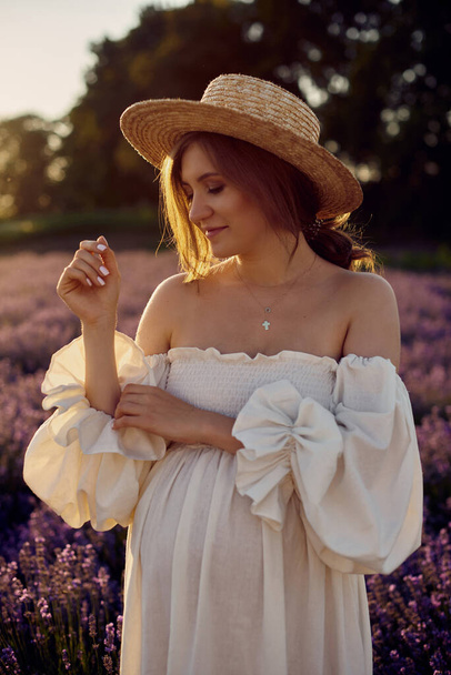 the pregnant girl with a hat in the lavender field on a sunset - Foto, afbeelding