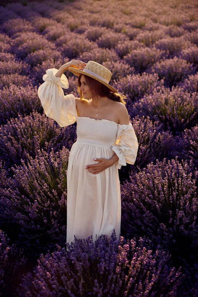 the pregnant girl with a hat in the lavender field on a sunset - Foto, Imagen