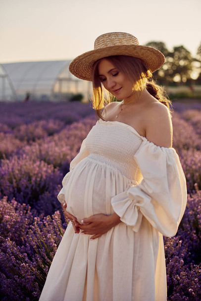 the pregnant girl with a hat in the lavender field on a sunset - Foto, Imagem
