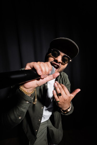 indian hip hop performer in sunglasses singing in microphone on black - 写真・画像