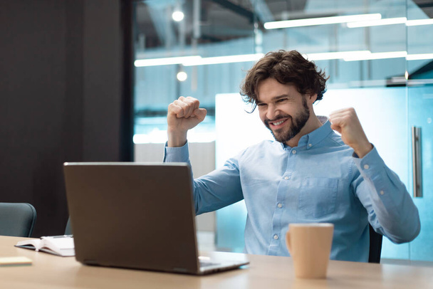 Excited mature businessman celebrating achievement, making great deal or agreement, gesturing YES near laptop at modern office, copy space. Achieving success, professional triumph concept - Photo, Image