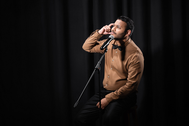 thoughtful indian comedian performing stand up comedy and telling jokes in microphone on black - Foto, immagini