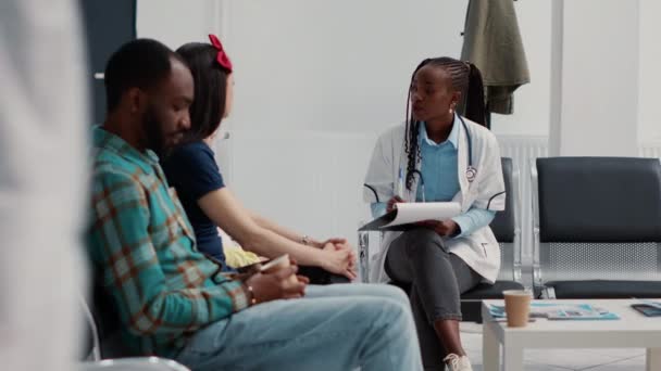 Αφροαμερικανός ειδικός κάνει ερωτήσεις σχετικά με την υγειονομική περίθαλψη για να συμβουλευτεί το κοριτσάκι με τη μητέρα στην αίθουσα αναμονής. Γιατρός μιλάει στο παιδί με τη μαμά για την ασθένεια και τη διάγνωση. - Πλάνα, βίντεο