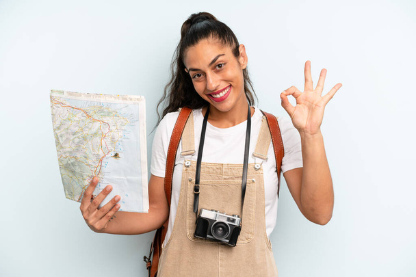 hispanic woman feeling happy, showing approval with okay gesture. tourist with a map - Foto, afbeelding