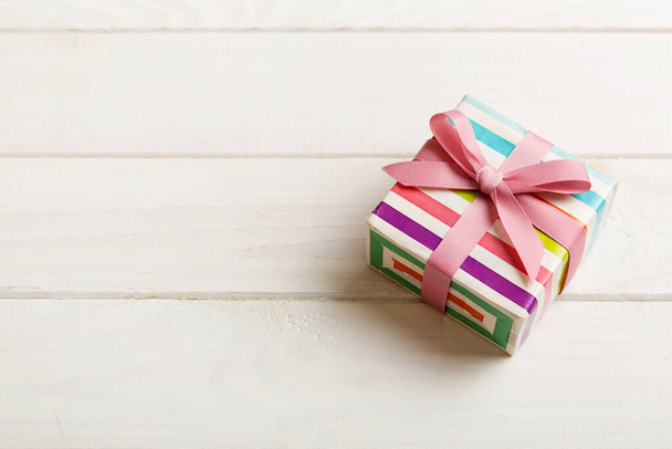 verpakt Kerstmis of andere vakantie handgemaakte geschenkdoos in kleur papier met lint op gekleurde achtergrond. Aanwezig doos, decoratie van geschenk op gekleurde tafel, bovenaanzicht met kopieerruimte. - Foto, afbeelding