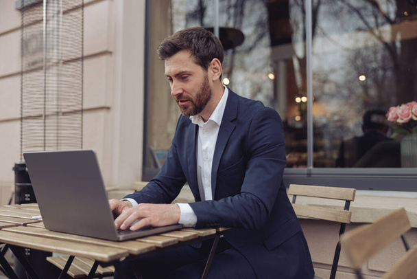 Homem bonito caucasiano trabalhando em laptop ao ar livre no café. A enviar mensagens no teclado. Conceito de negócio. - Foto, Imagem