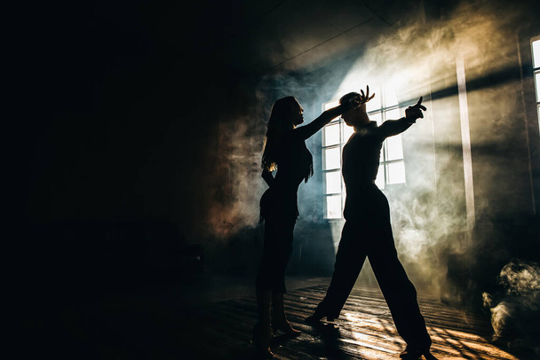 Δυο επαγγελματίες χορευτές χορεύουν στο στούντιο της σοφίτας. Όμορφη καλλιτεχνική παράσταση με βαρύ καπνό. Αθλητική ζωή έννοια. Πάθος και συναισθηματικός χορός. - Φωτογραφία, εικόνα