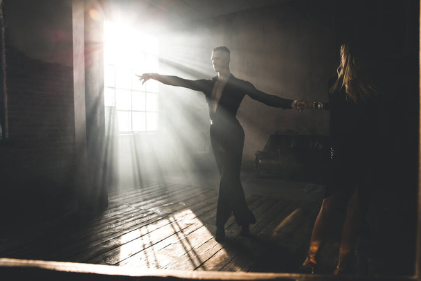Soft focused photo. Couple of two professional ballroom dancers is dancing on loft studio. Beautiful art performance with heavy smoke. Sport life concept. Passion and emotional dance. - 写真・画像