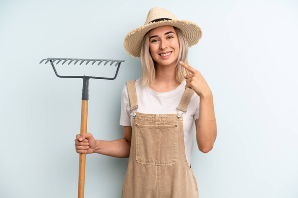 blonde woman smiling confidently pointing to own broad smile. farmer and rake cocnept - Фото, зображення