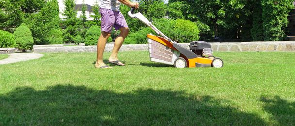 Muž sekající trávník sekačkou v létě. Jarní sezóna slunečné sekání trávníku v zahradě - Fotografie, Obrázek