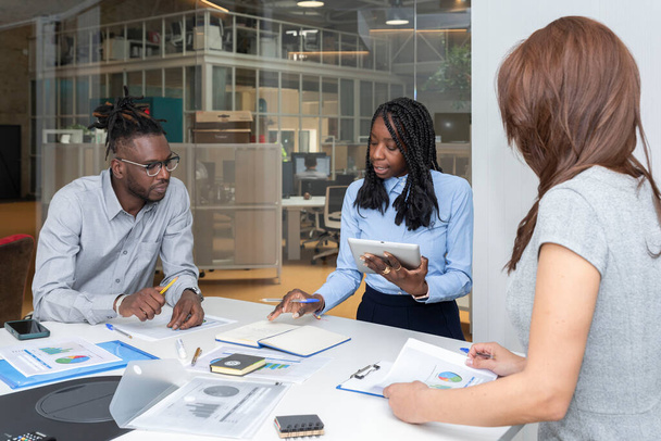 trois jeunes entrepreneurs multiraciaux avec une tablette numérique et des graphiques sur la table préparant la stratégie d'entreprise - Photo, image