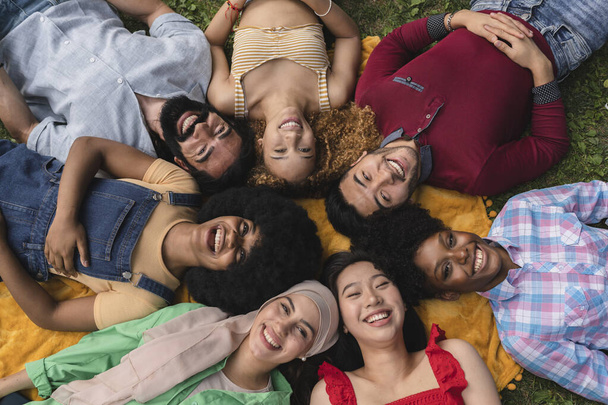 Eine lächelnde Gruppe multiethnischer Freunde liegt im Kreis auf dem Rasen. - Picknick-Konzept - - Foto, Bild