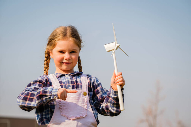 Child playing and looks interested at a wind turbine toy - Concept of future generation and enewable Energy - Foto, Imagen