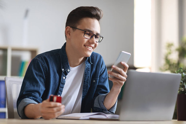 Smiling Young Office Worker Holding Credit Card And Smartphone, Making Order Online While Sitting At Workplace, Smiling Millennial Employee Enjoying Intesnet Shopping And E-Commerce, Closeup - Foto, Imagem