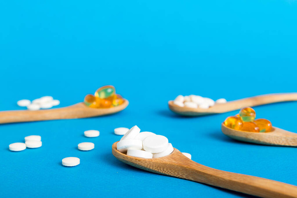 Vitamine capsules in een lepel op een gekleurde achtergrond. Pillen dienden als een gezonde maaltijd. Rode zachte gel vitamine supplement capsules op lepel. - Foto, afbeelding