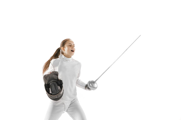 Winner emotions. Portrait of young charming girl, fencer in white fencing costume posing with rapier isolated on white background. Sport, youth, hobbies, achievements, goal. - Φωτογραφία, εικόνα