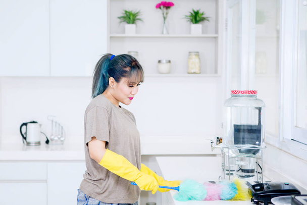 Portrait of young woman cleaning table with a duster brush and standing in the kitchen at home - Photo, Image