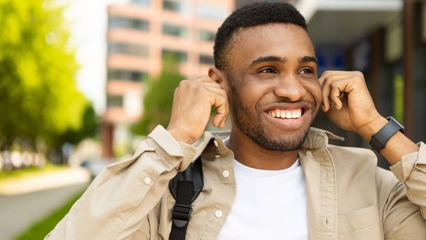 市内の屋外を歩くワイヤレスヘッドフォンで音楽を聴く幸せな黒人のクローズアップ肖像画。高品質の写真 - 写真・画像