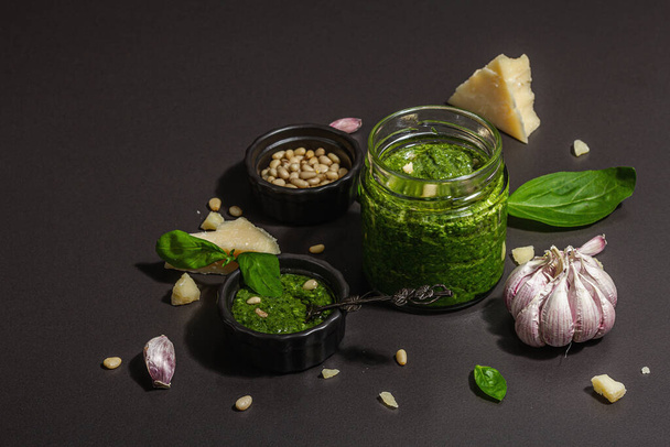 Klassisch italienische Basilikum-Pesto-Sauce im Glas. Hausgemachtes Essen, Zutaten für ein traditionelles Rezept. Hartes Licht, dunkler Schatten, schwarzer Steinhintergrund, Kopierraum - Foto, Bild