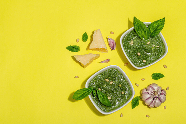 Pesto sauce in a bowls with pine nuts, parmesan and garlic. Trendy hard light, dark shadow, bright yellow background - 写真・画像