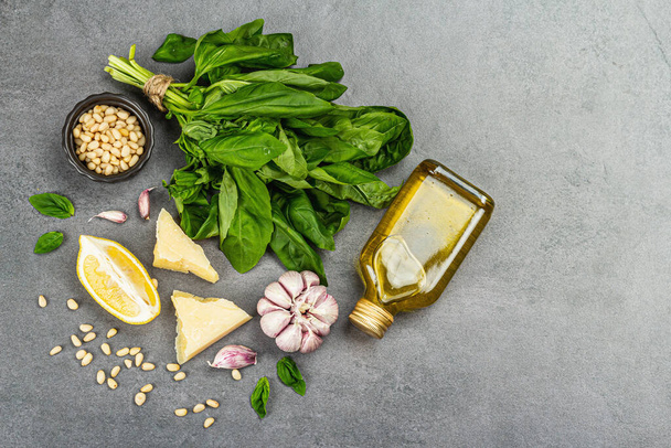 Traditional ingredients for the preparation of classic Italian basil pesto. Fresh leaves, olive oil, parmesan, garlic, and pine nuts. Vegan healthy food, grey stone concrete background, top view - Photo, image