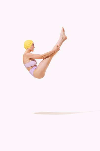 Portrait of young woman in swimming suit and cap jumping into water isolated over grey studio background. Gymnast. Concept of beauty, fashion, vintage style, summertime, party. Copy space for ad - Fotó, kép