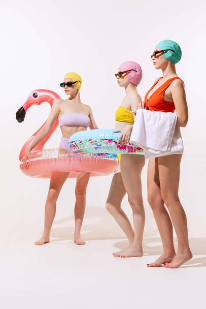 Portrait of young women in swimming suit, cap and sunglasses posing with swimming circle isolated over grey studio background. Beach party Concept of beauty, fashion, vintage style, summertime, party. - Fotografie, Obrázek