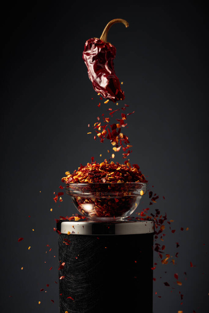 Dried red pepper crumbles into flakes and falls into a small glass bowl. - Photo, Image