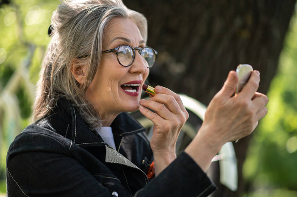 Beauty. A mature woman in eyeglasses doing make up - Фото, зображення